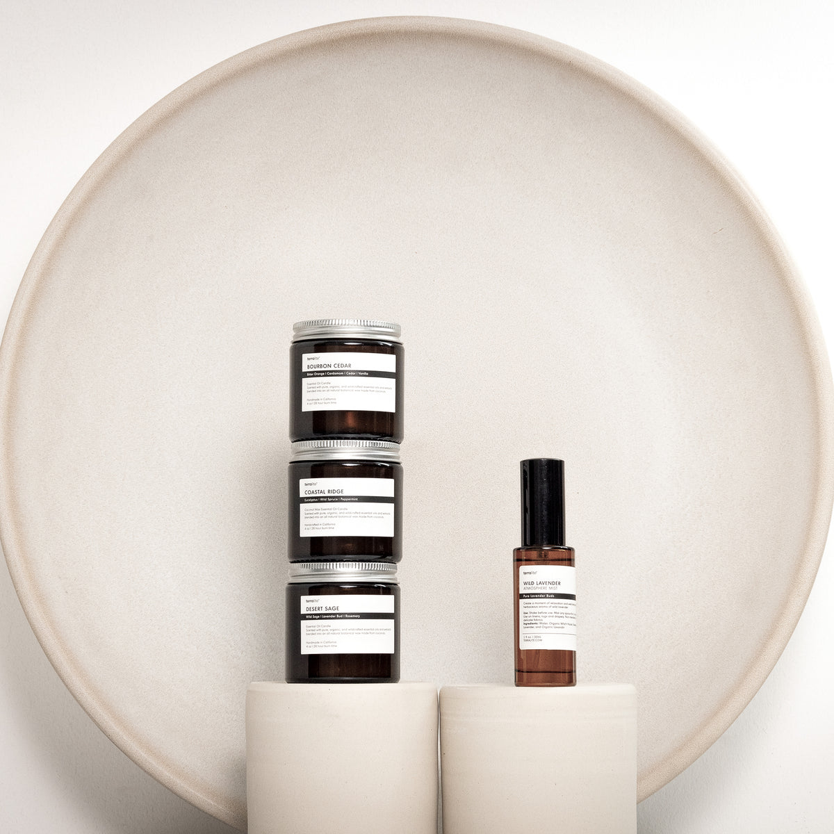 Three Terralite travel candles stacked beside the Wild Lavender atmosphere mist, in front of a stoneware plate
